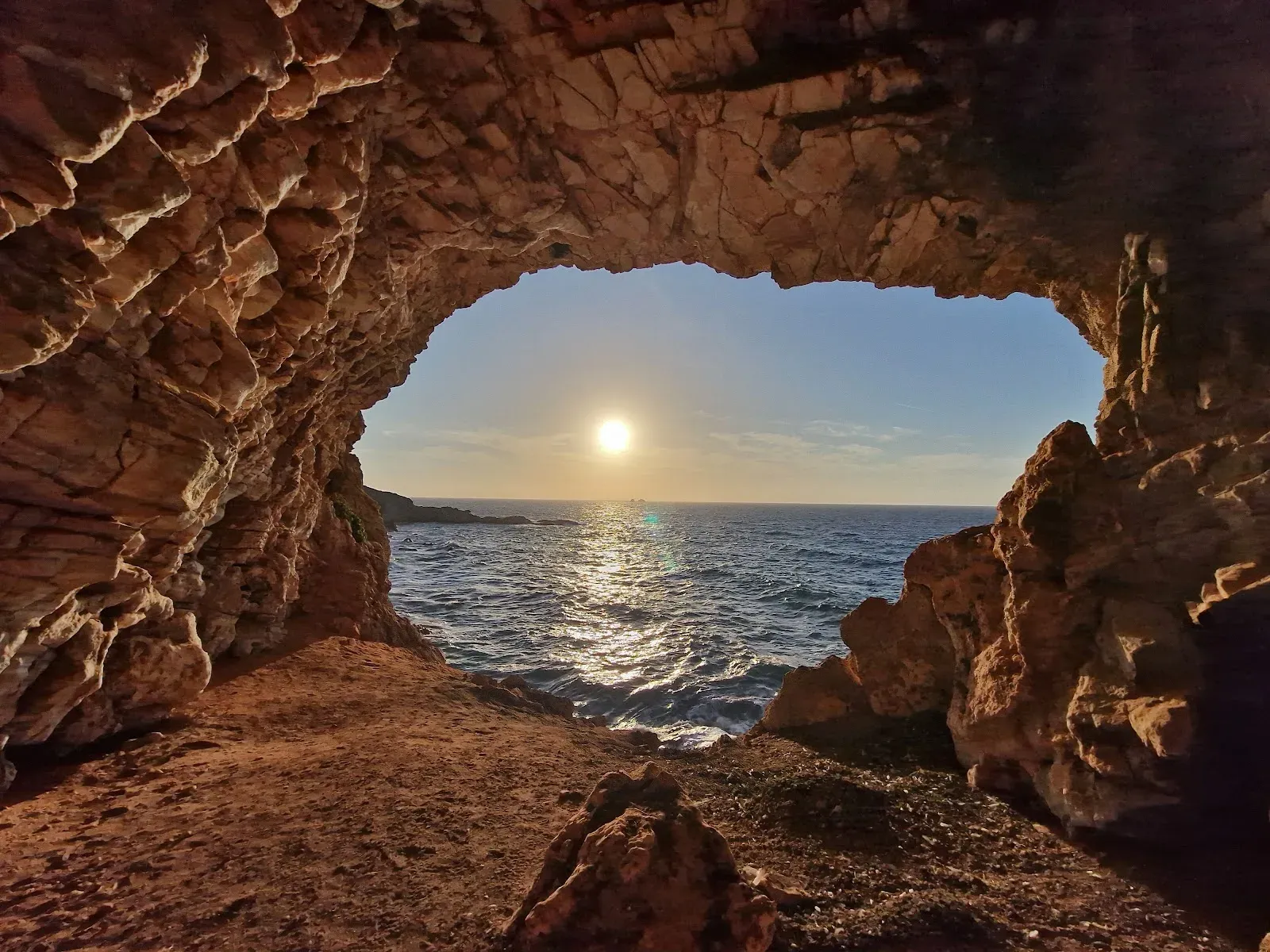 The sun setting through a sea cave on the coast of Paros